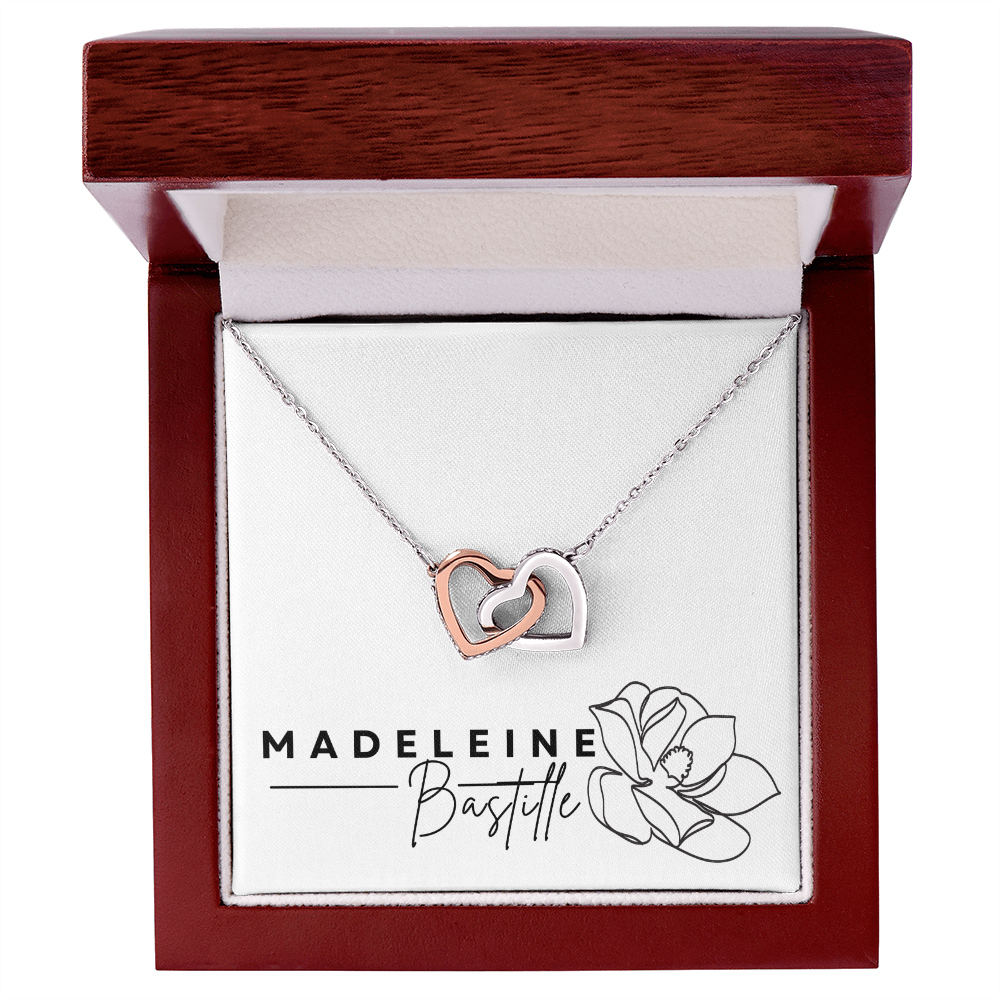 An interlocking hearts necklace with cubic zirconia crystals, presented in a box with 'MADELEINE BASTILLE' branding and a floral design.