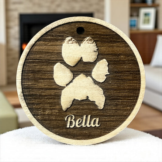 Wooden ornament with paw print design and 'Bella' engraving on a blurred indoor background