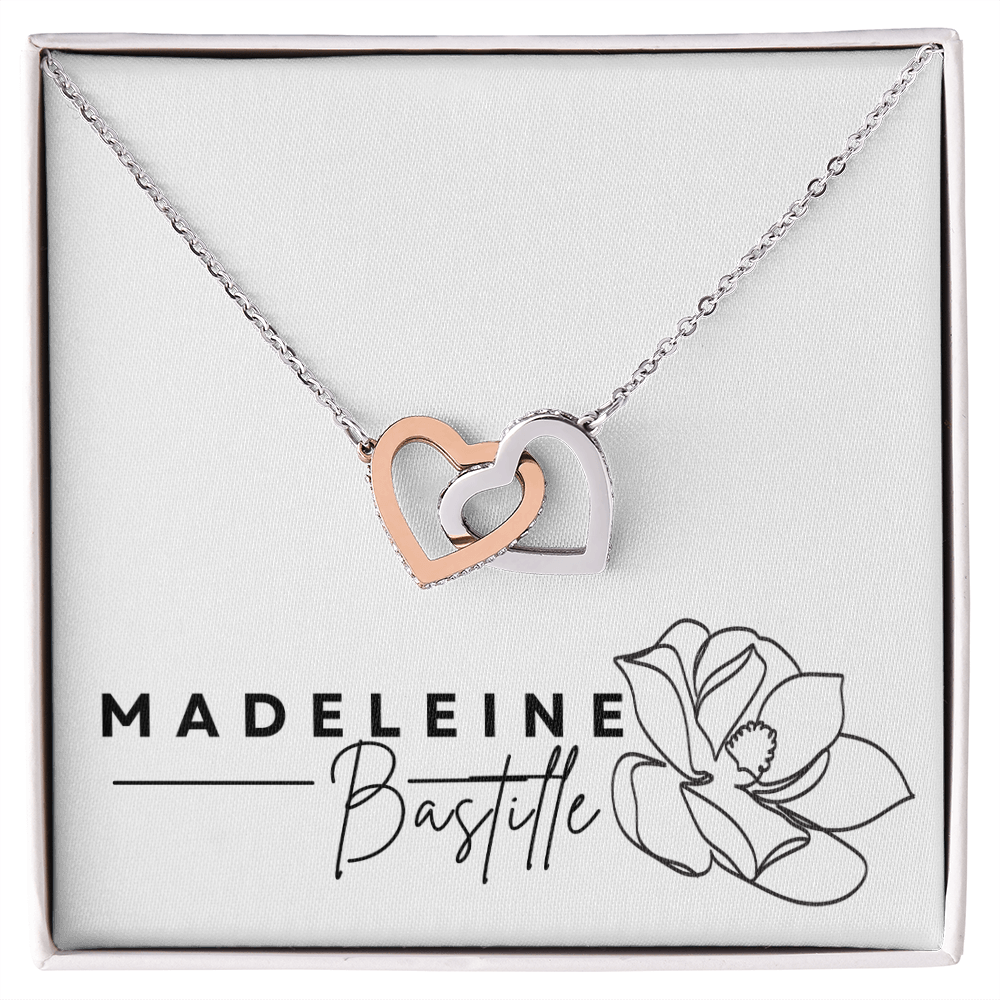 An interlocking hearts necklace with cubic zirconia crystals, presented in a box with 'MADELEINE BASTILLE' branding and a floral design.